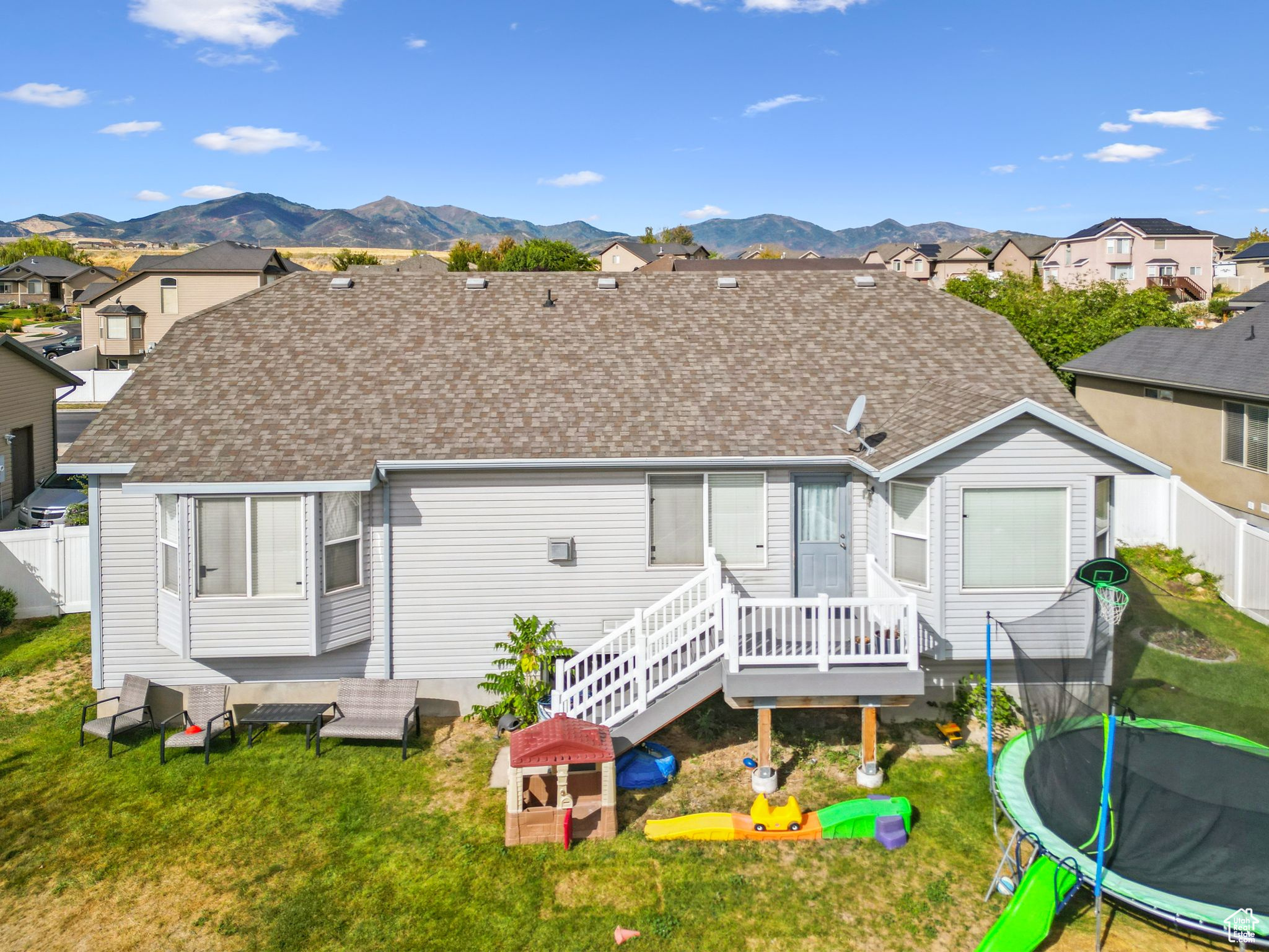 Rear view of house with a lawn, a trampoline, fence, a residential view, and a shingled roof