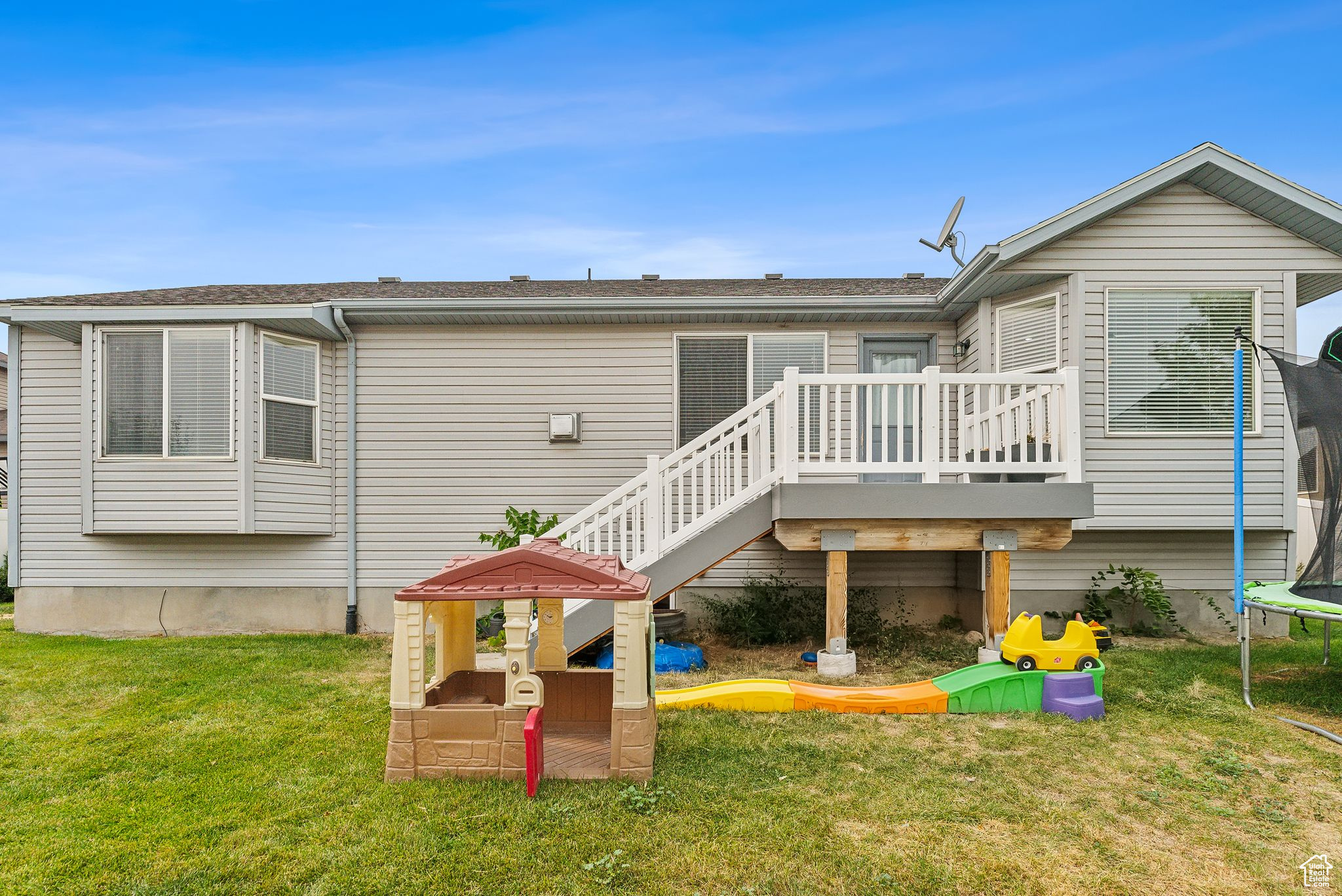 Back of property with a yard, a trampoline, a deck, and stairs