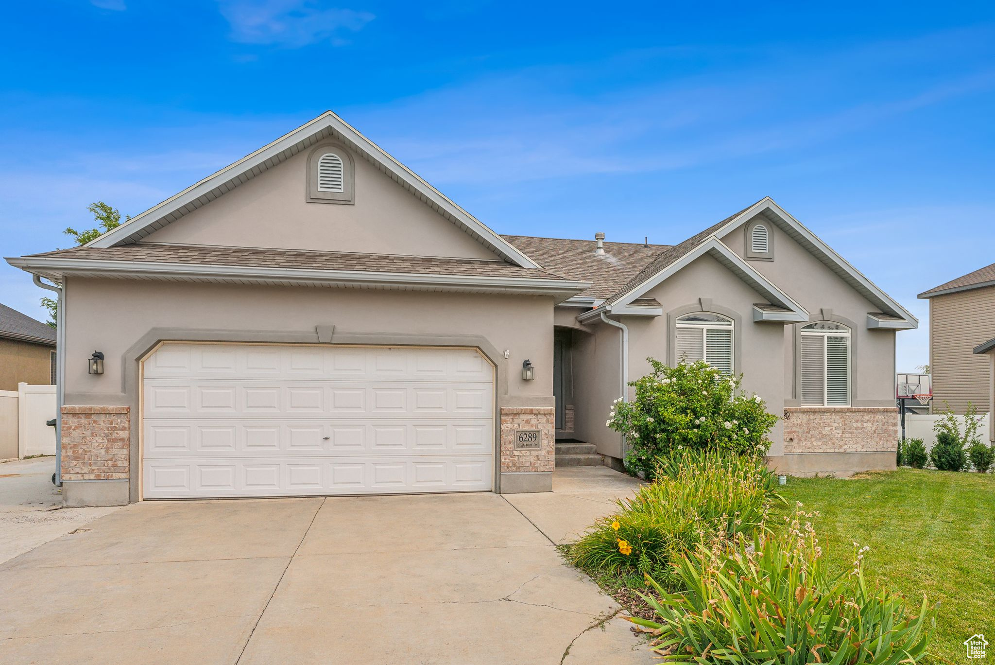 Ranch-style house with brick siding, a front yard, stucco siding, a garage, and driveway