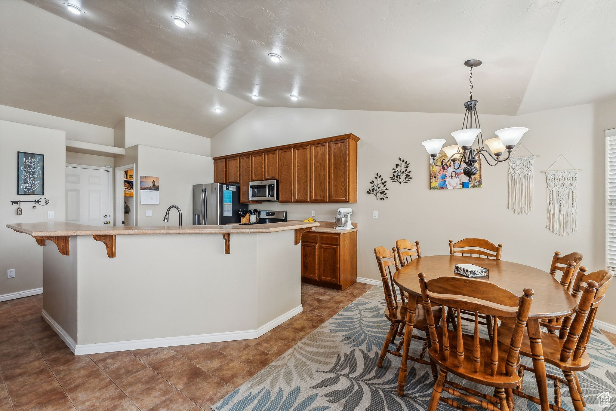 Kitchen with a kitchen bar, brown cabinets, stainless steel appliances, light countertops, and lofted ceiling