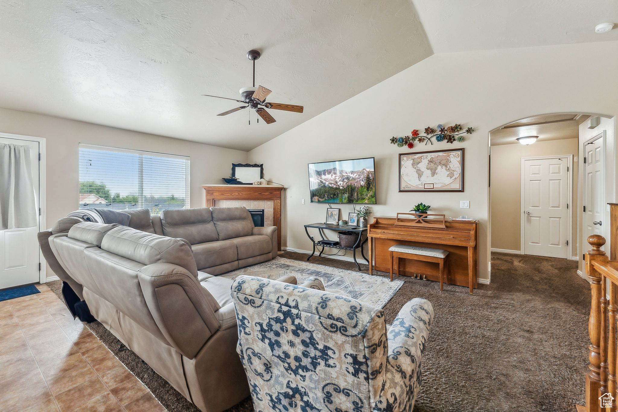 Living area with lofted ceiling, a ceiling fan, arched walkways, baseboards, and light colored carpet