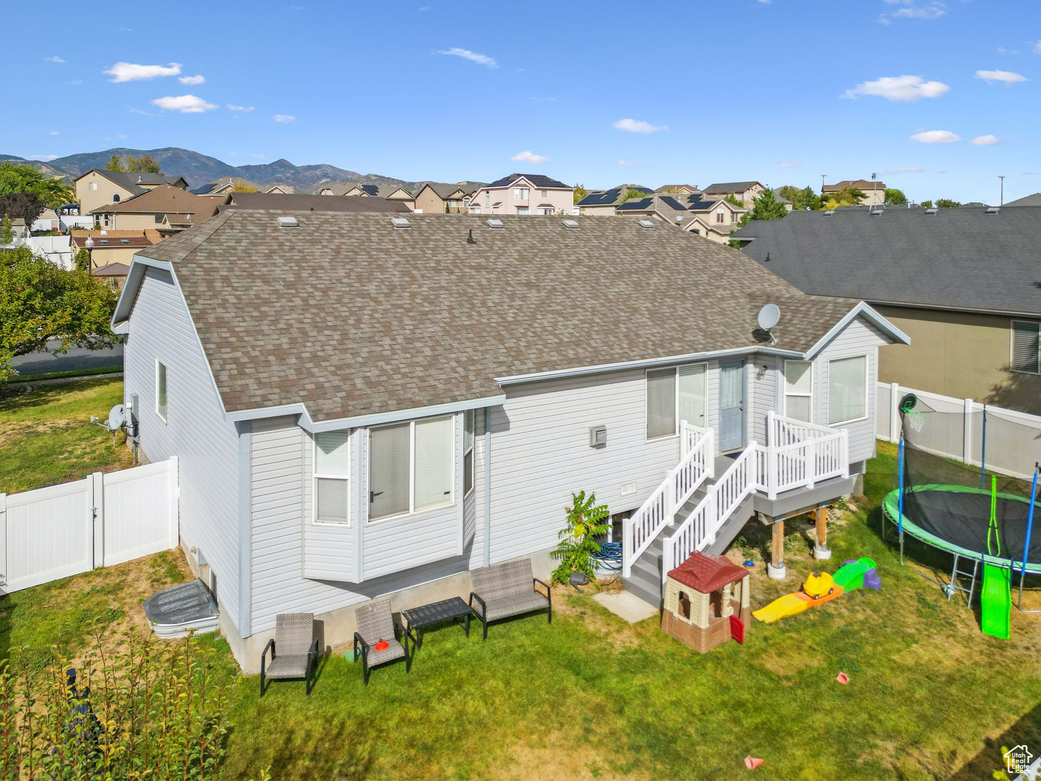 Back of house featuring a gate, roof with shingles, a yard, a trampoline, and a mountain view