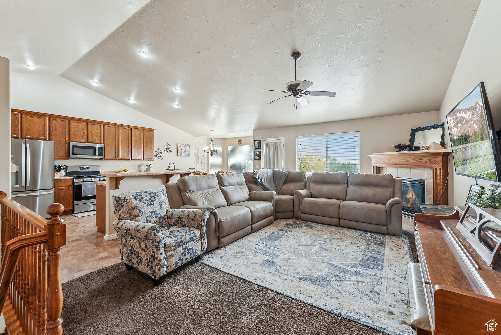 Living room featuring a tiled fireplace, ceiling fan with notable chandelier, and lofted ceiling