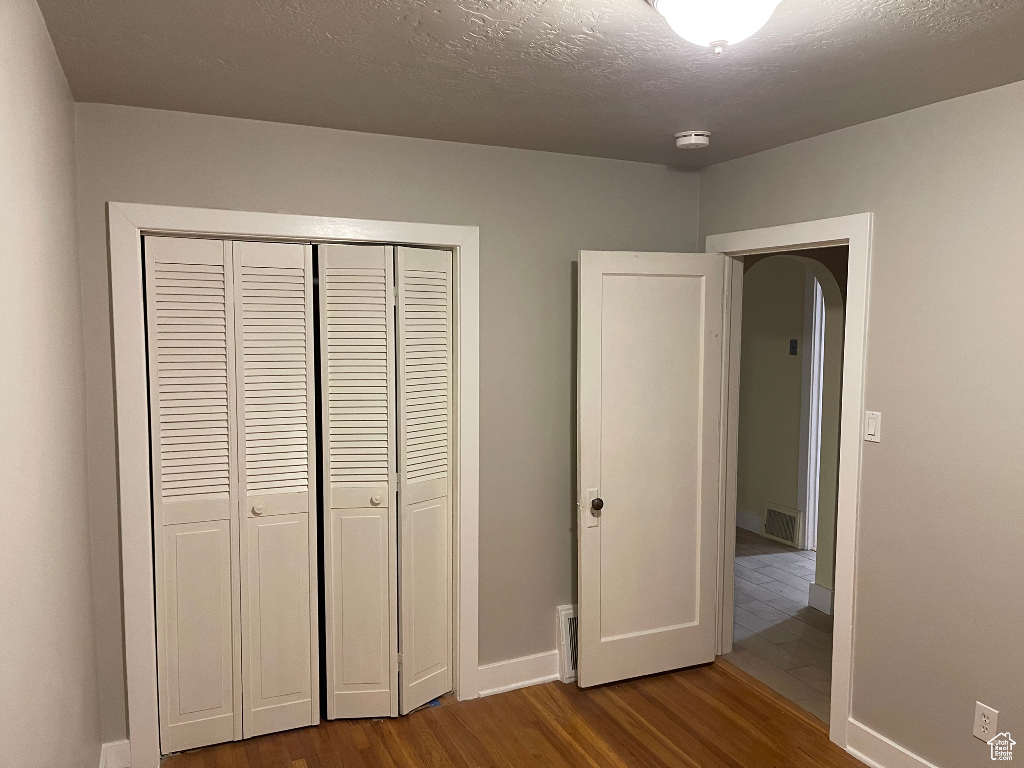 Unfurnished bedroom featuring a textured ceiling, a closet, baseboards, and dark wood-type flooring