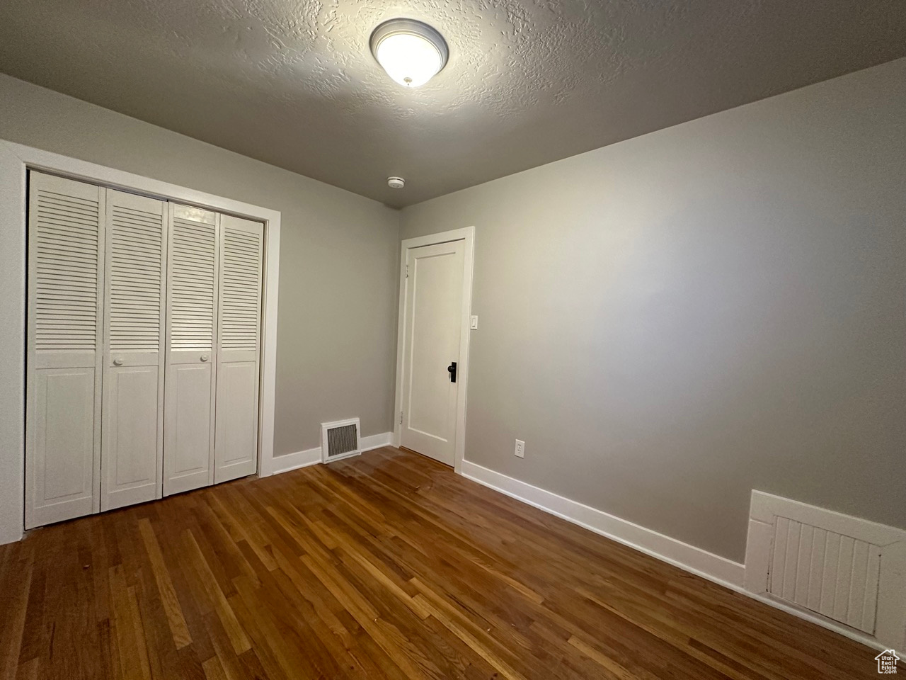Unfurnished bedroom featuring dark wood-style flooring, visible vents, and baseboards