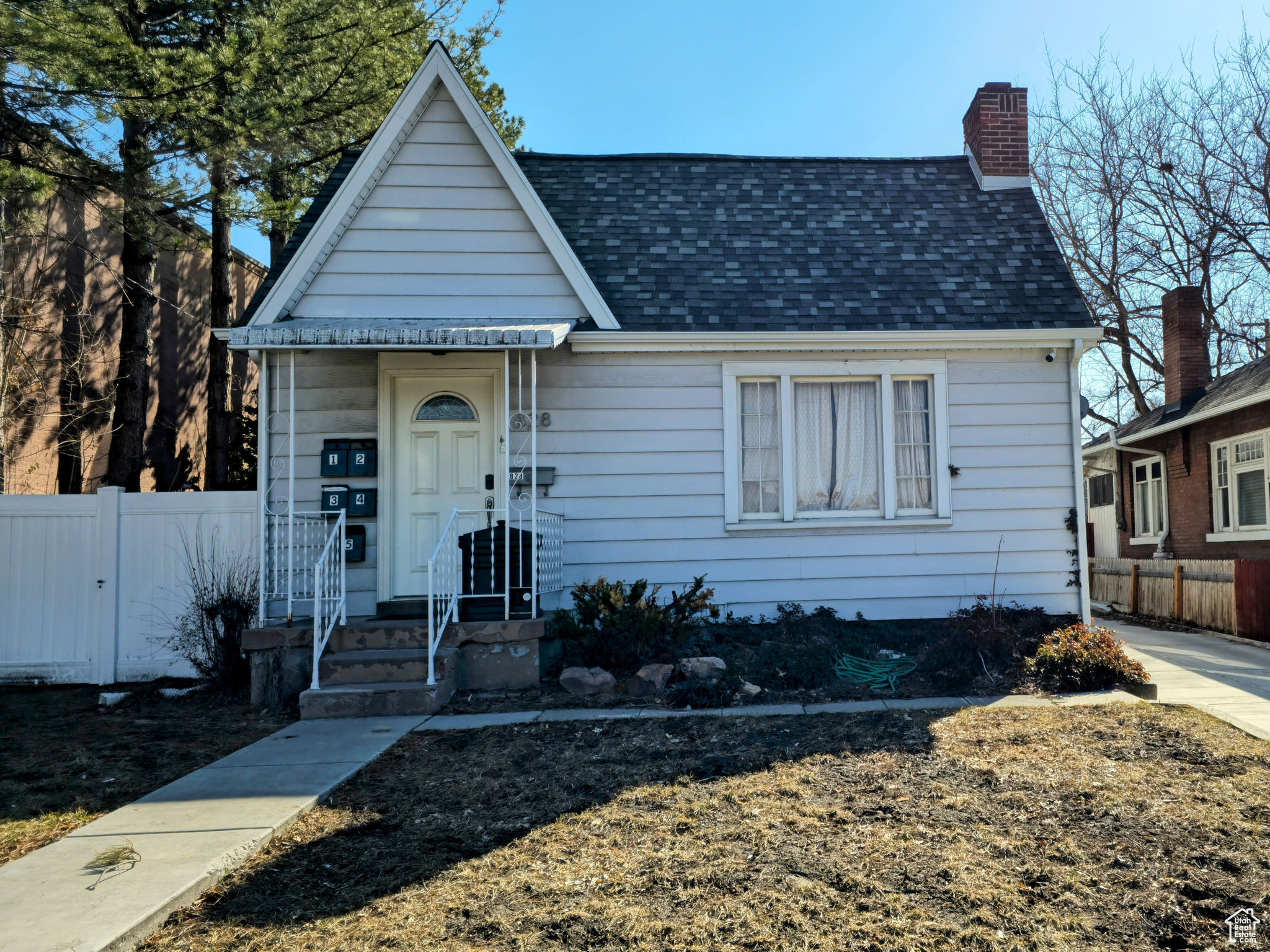 View of front of house featuring a shingled roof, a chimney, and fence