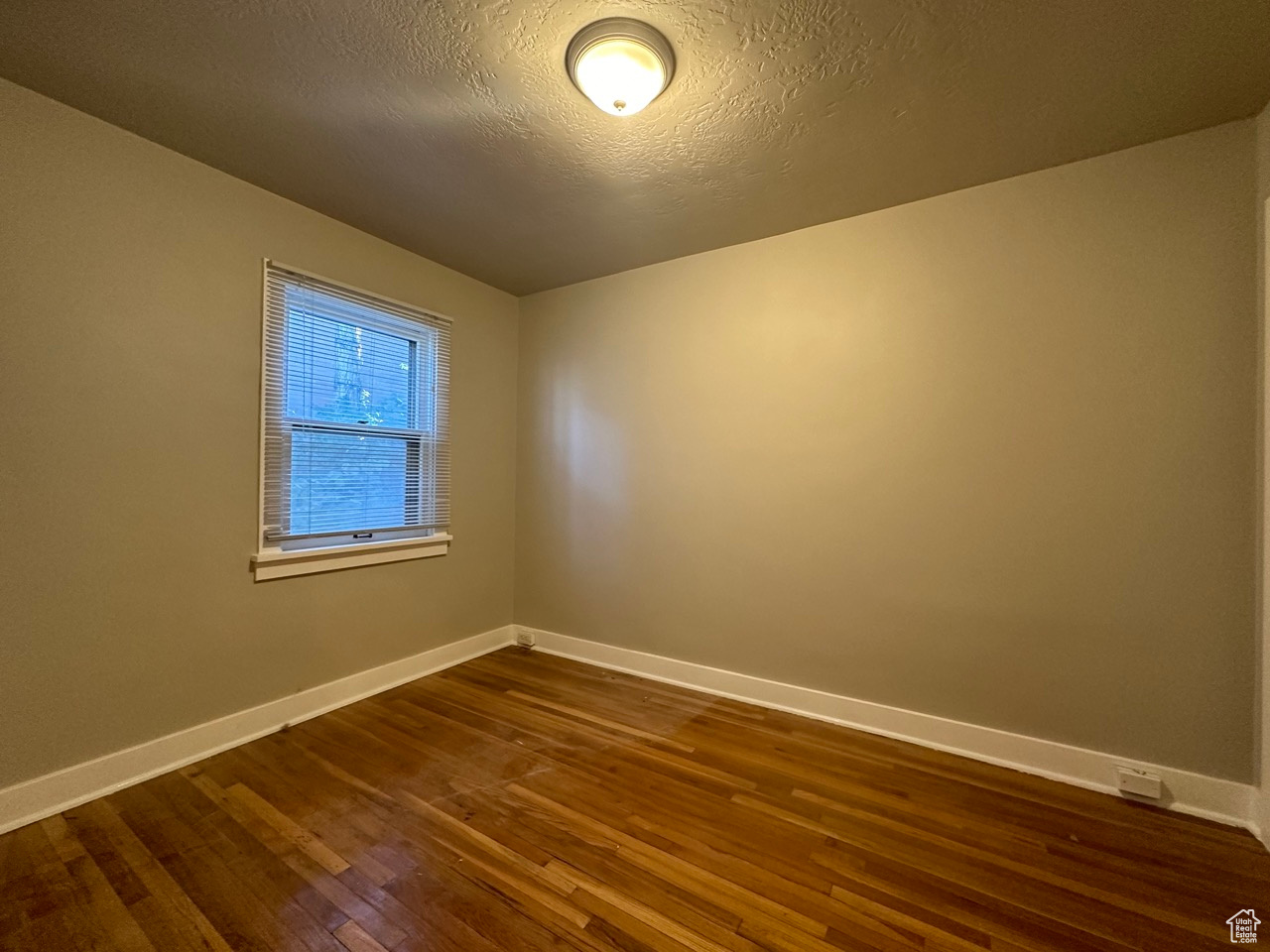 Empty room with dark wood-style flooring, a textured ceiling, and baseboards