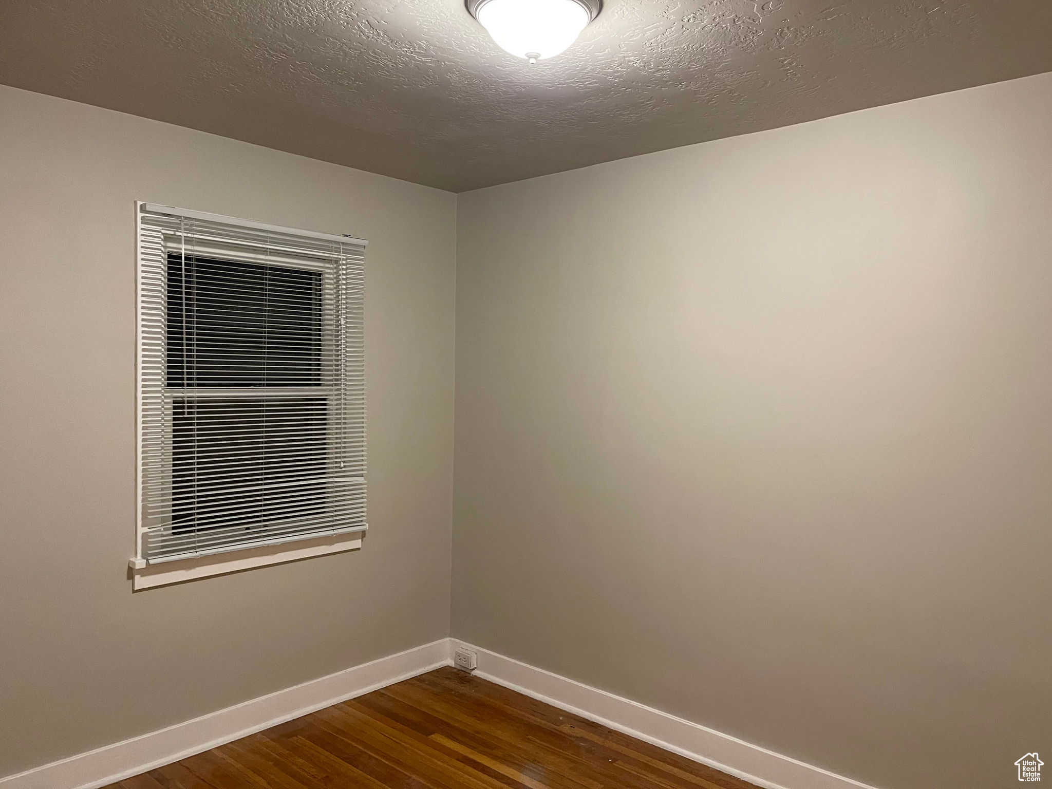 Empty room with dark wood-style floors, baseboards, and a textured ceiling