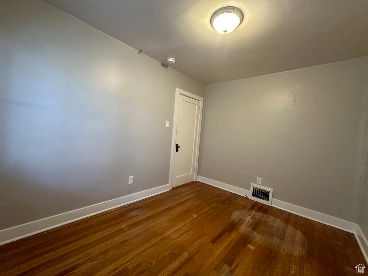 Unfurnished room featuring dark wood-style flooring, visible vents, and baseboards