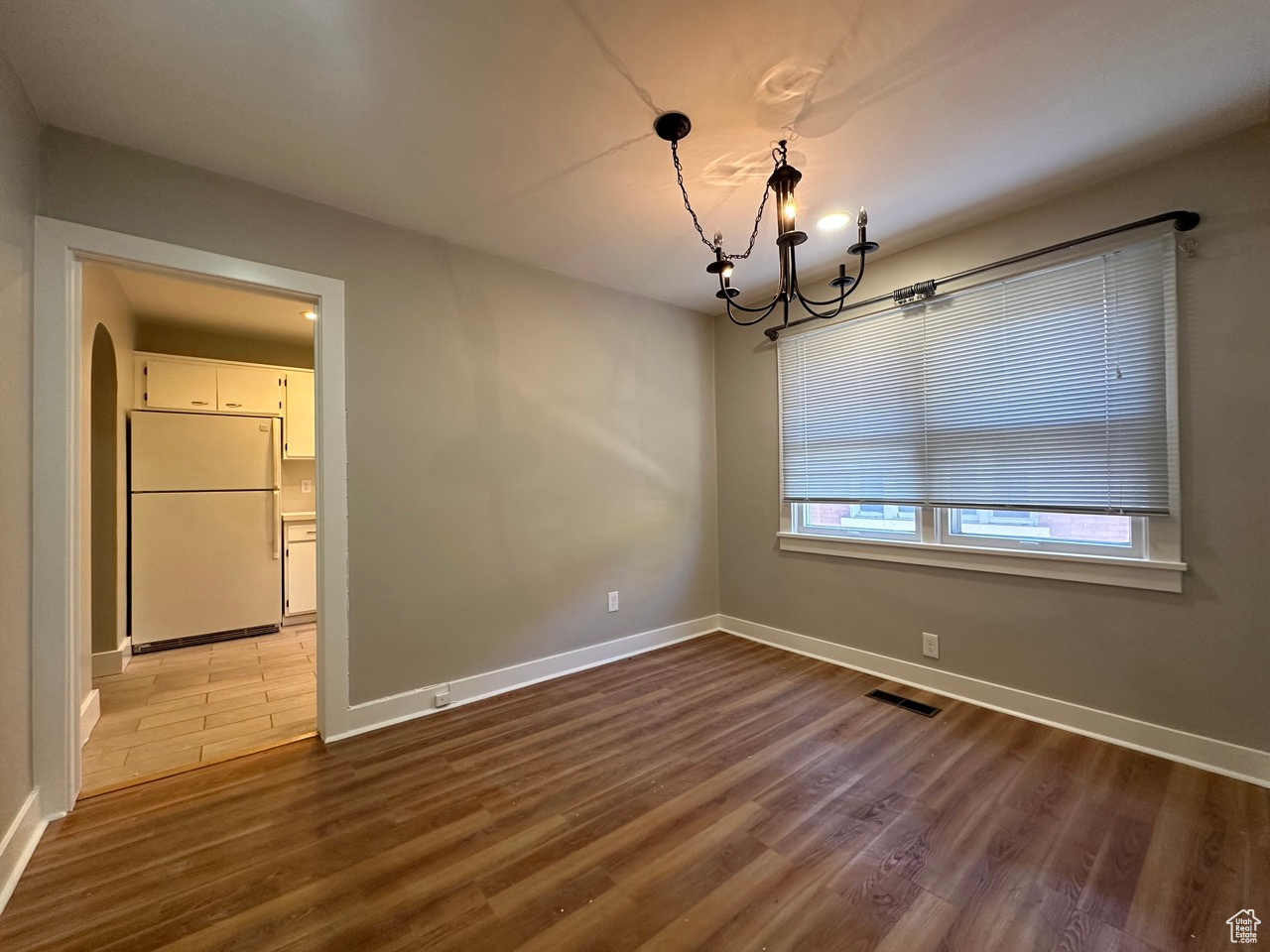 Unfurnished dining area with arched walkways, a notable chandelier, wood finished floors, visible vents, and baseboards
