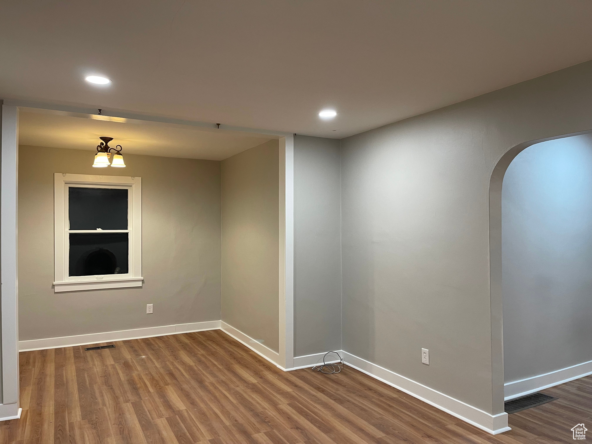 Unfurnished room with baseboards, visible vents, arched walkways, and wood finished floors