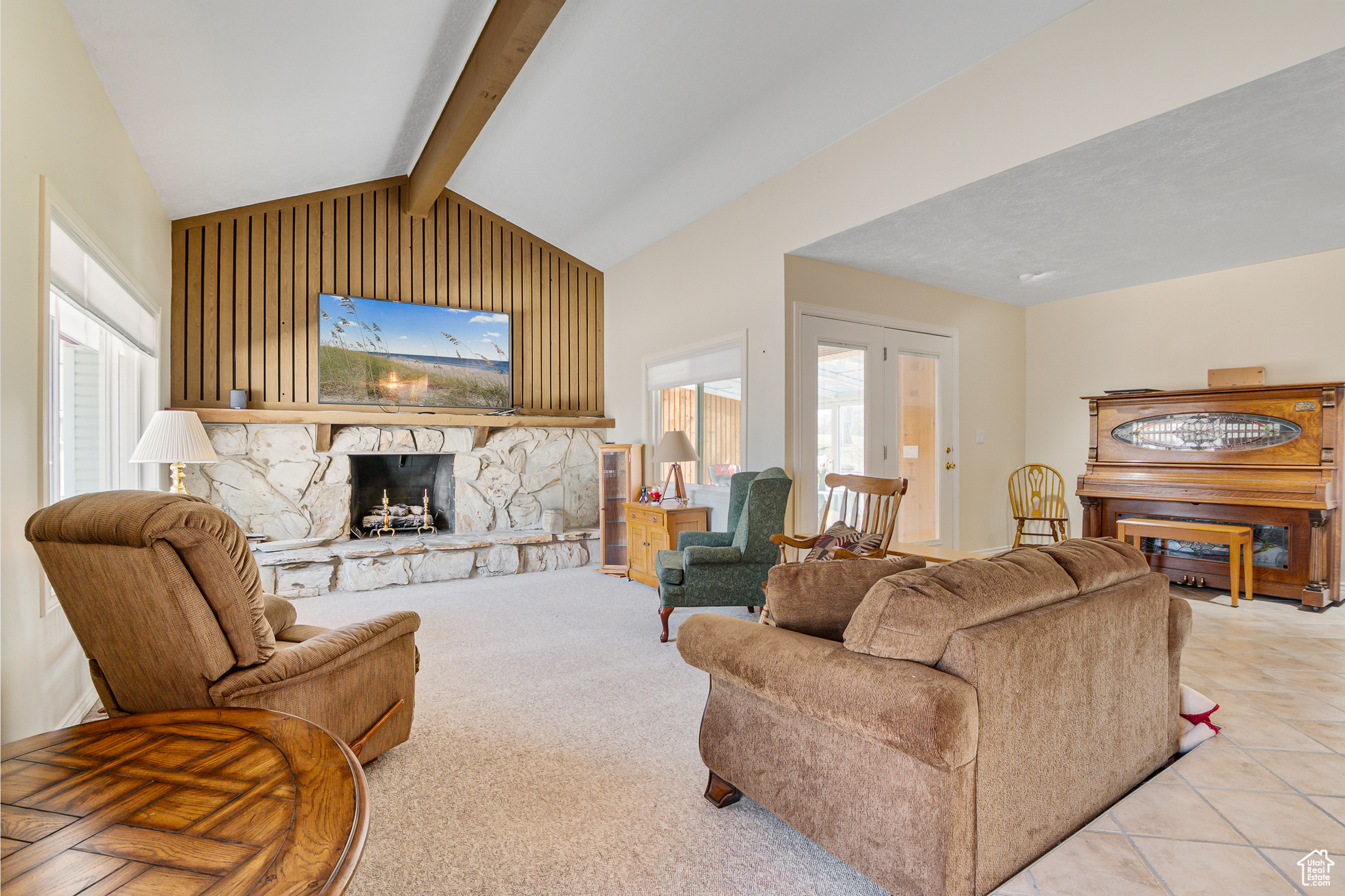 Living Room featuring a stone fireplace, vaulted ceiling with beam, and tile flooring