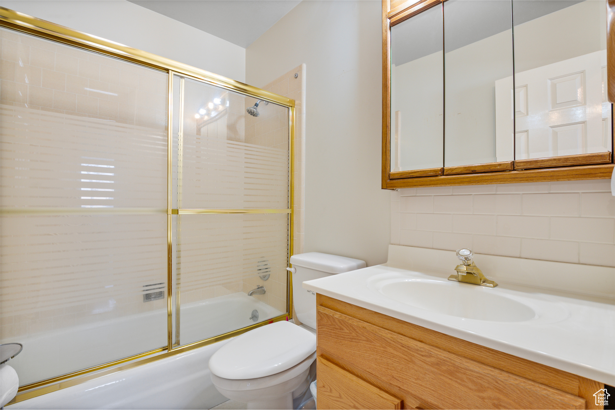 Full bath with vanity, backsplash, shower / bath combination with glass door, and toilet