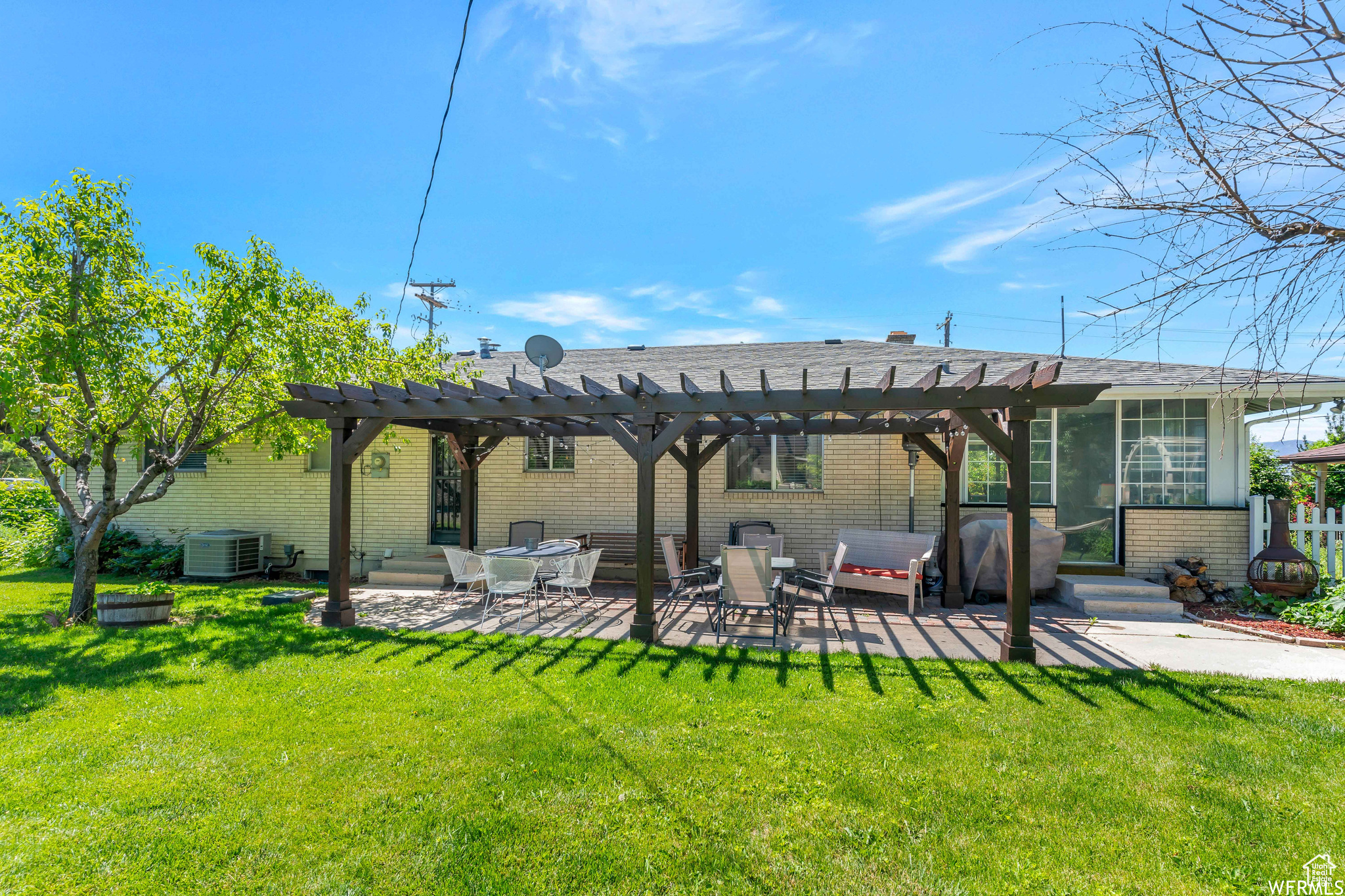 Rear view of house featuring brick siding, central AC unit, a lawn, a patio area, and a pergola