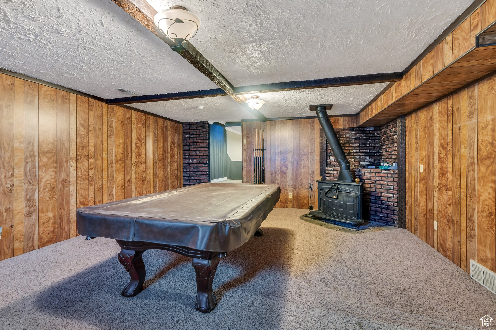 Recreation room featuring carpet floors, a textured ceiling, wood walls, and a wood stove