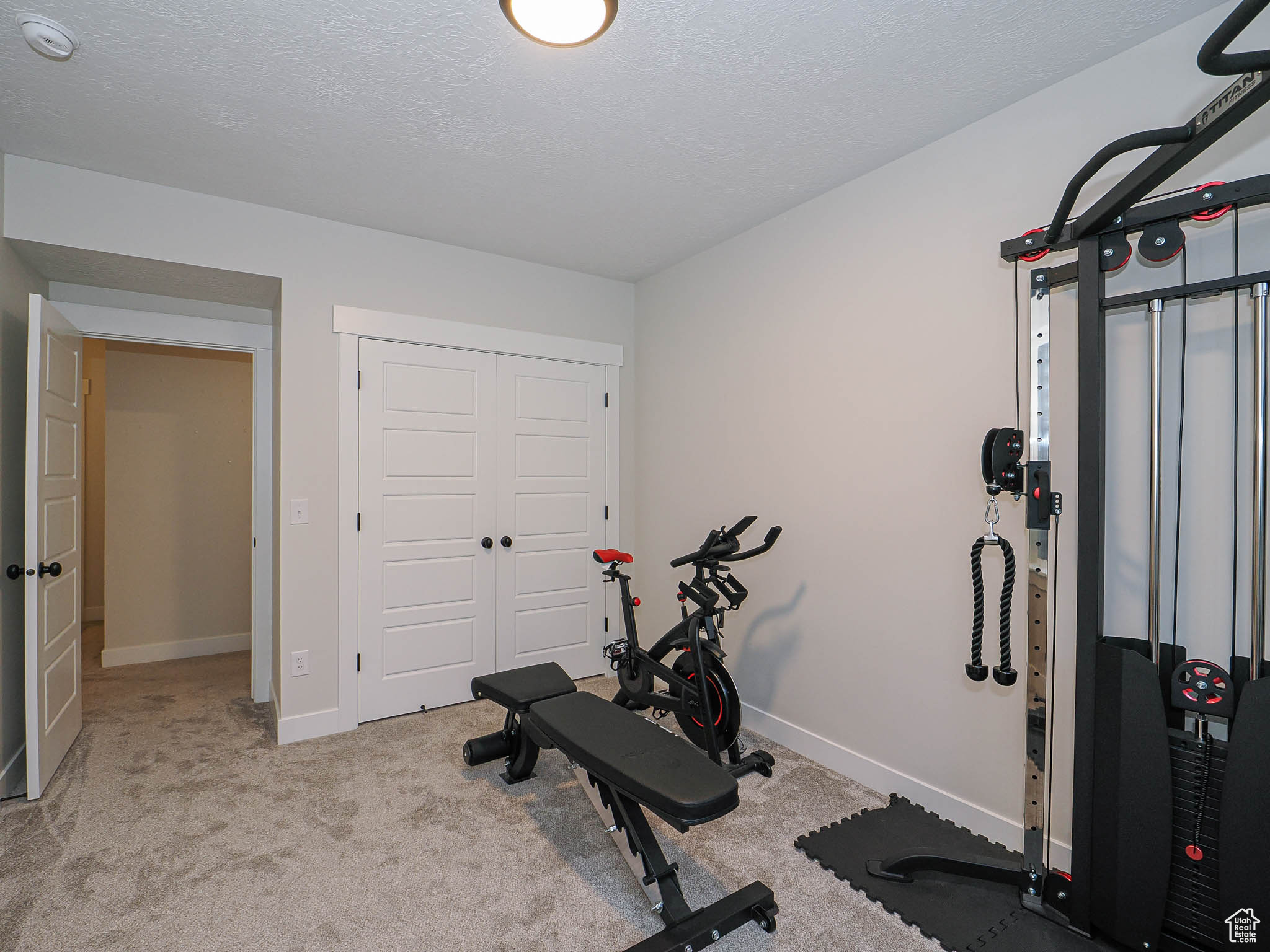Exercise area with light carpet, baseboards, and a textured ceiling
