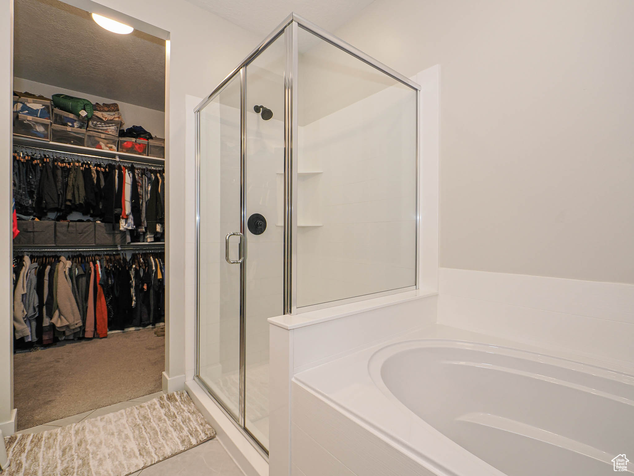 Bathroom featuring a shower stall, a textured ceiling, a walk in closet, and a bath