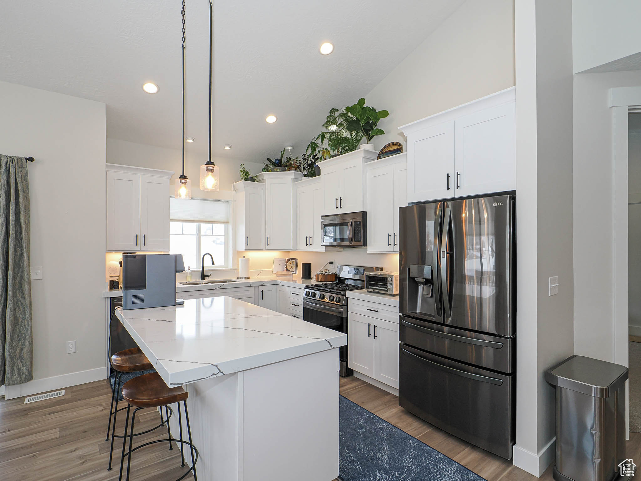 Kitchen with appliances with stainless steel finishes, white cabinets, a sink, and a center island