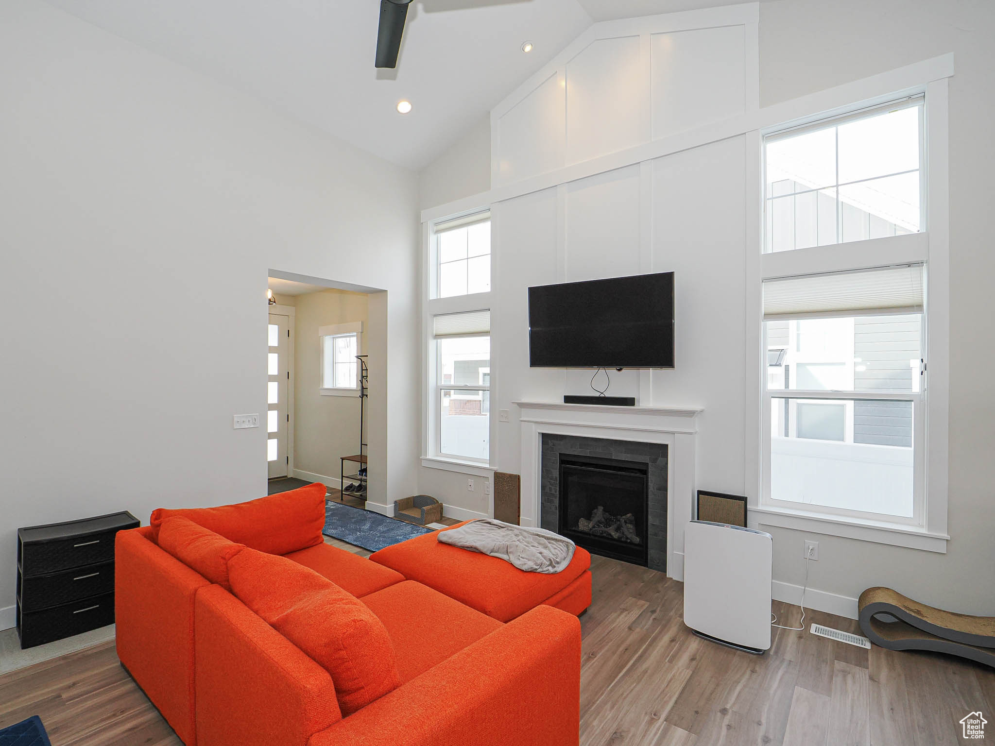 Living area featuring baseboards, a ceiling fan, wood finished floors, a fireplace, and high vaulted ceiling