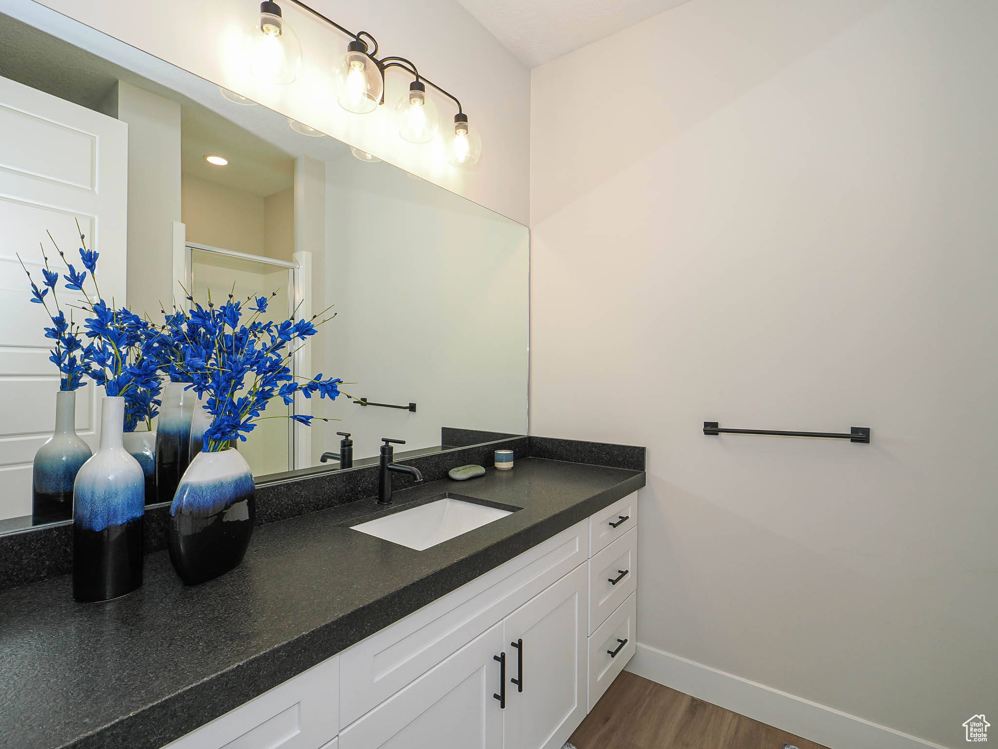 Bathroom featuring walk in shower, vanity, baseboards, and wood finished floors
