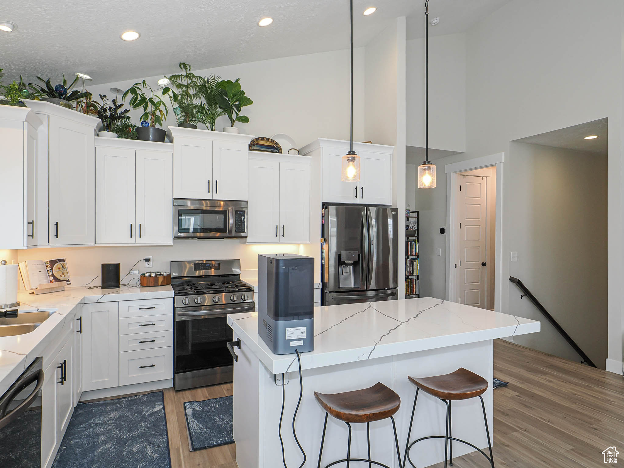 Kitchen with a center island, stainless steel appliances, hanging light fixtures, white cabinets, and wood finished floors