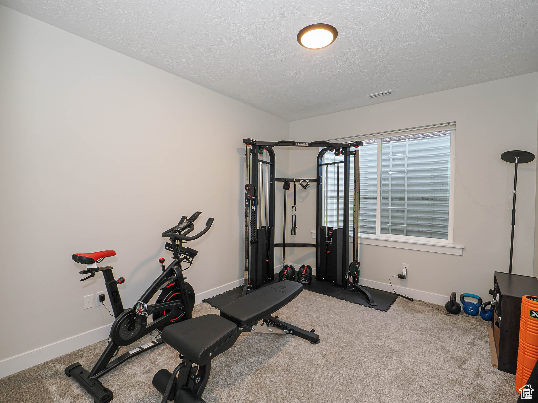 Workout area featuring light carpet, visible vents, baseboards, and a textured ceiling