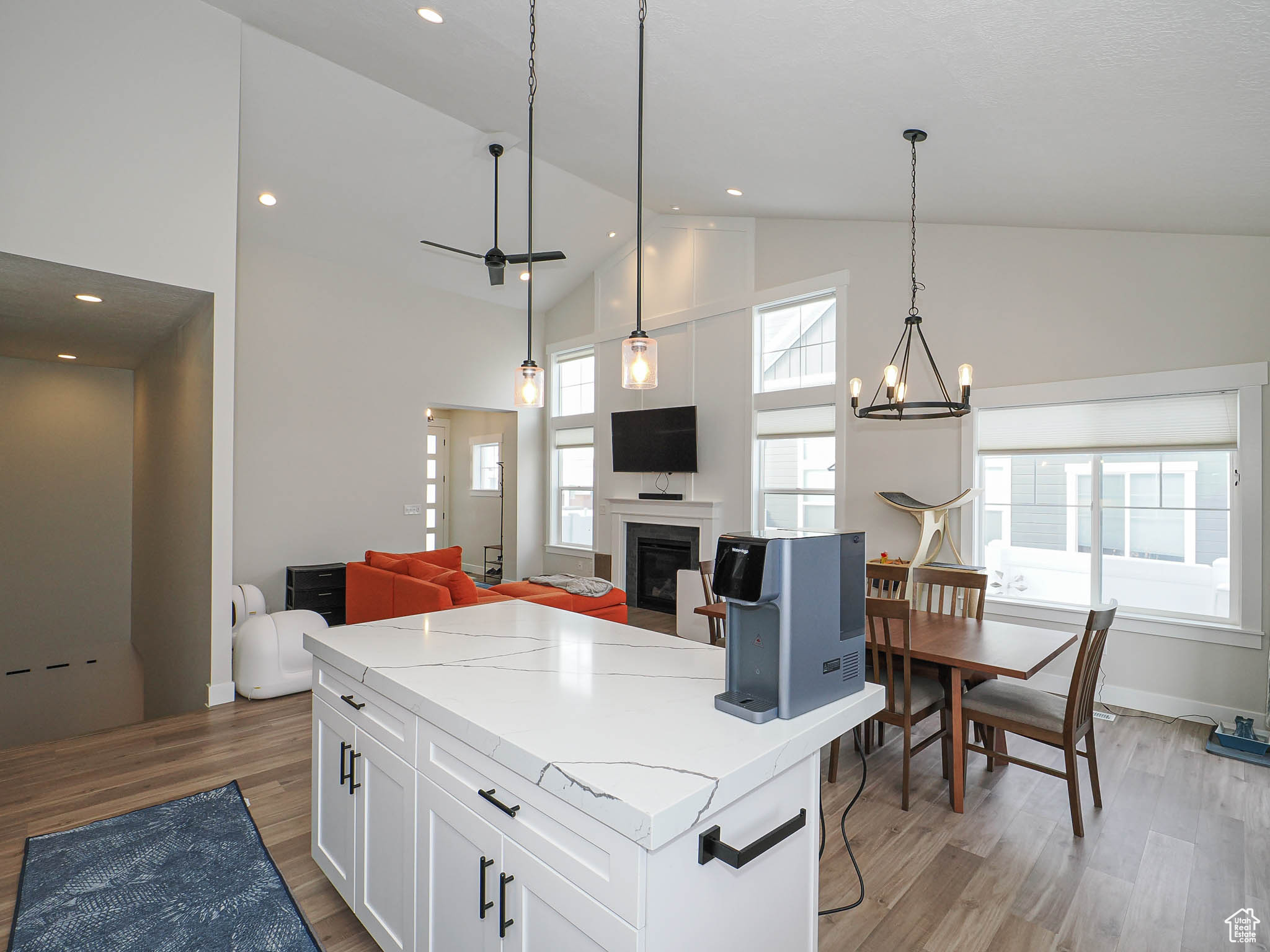 Kitchen with wood finished floors, white cabinets, open floor plan, light stone countertops, and pendant lighting