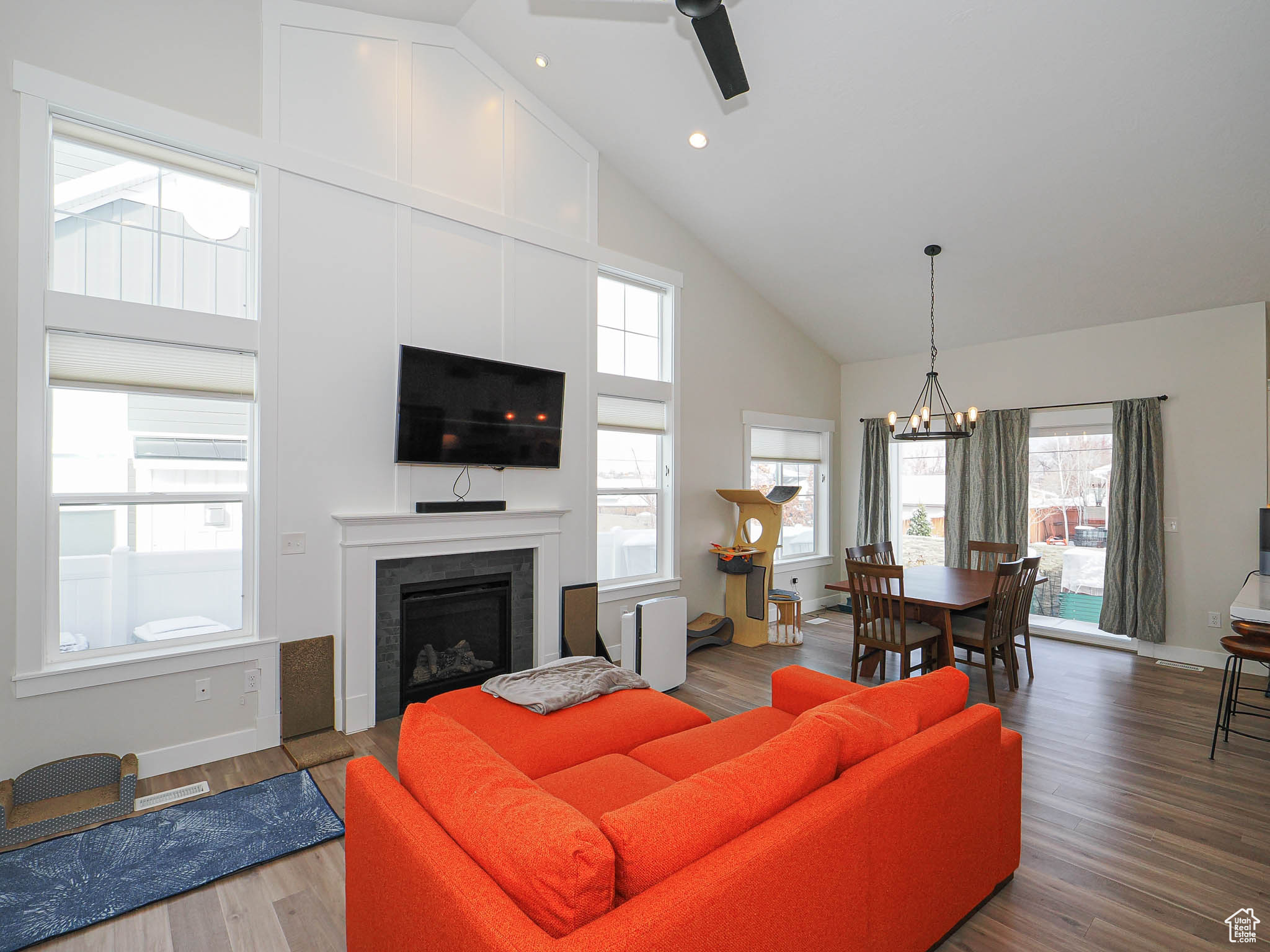 Living room with baseboards, wood finished floors, a fireplace, high vaulted ceiling, and ceiling fan with notable chandelier