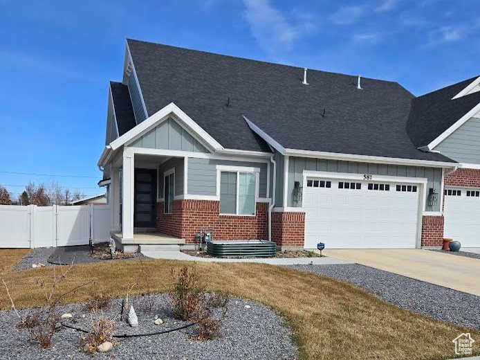 View of front facade featuring fence, an attached garage, concrete driveway, board and batten siding, and brick siding