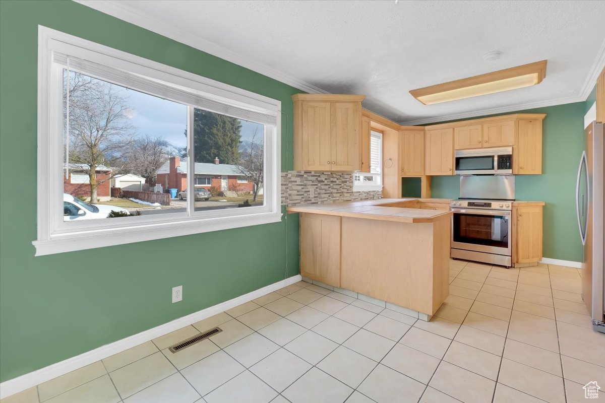 Kitchen with a peninsula, crown molding, light brown cabinetry, and stainless steel appliances