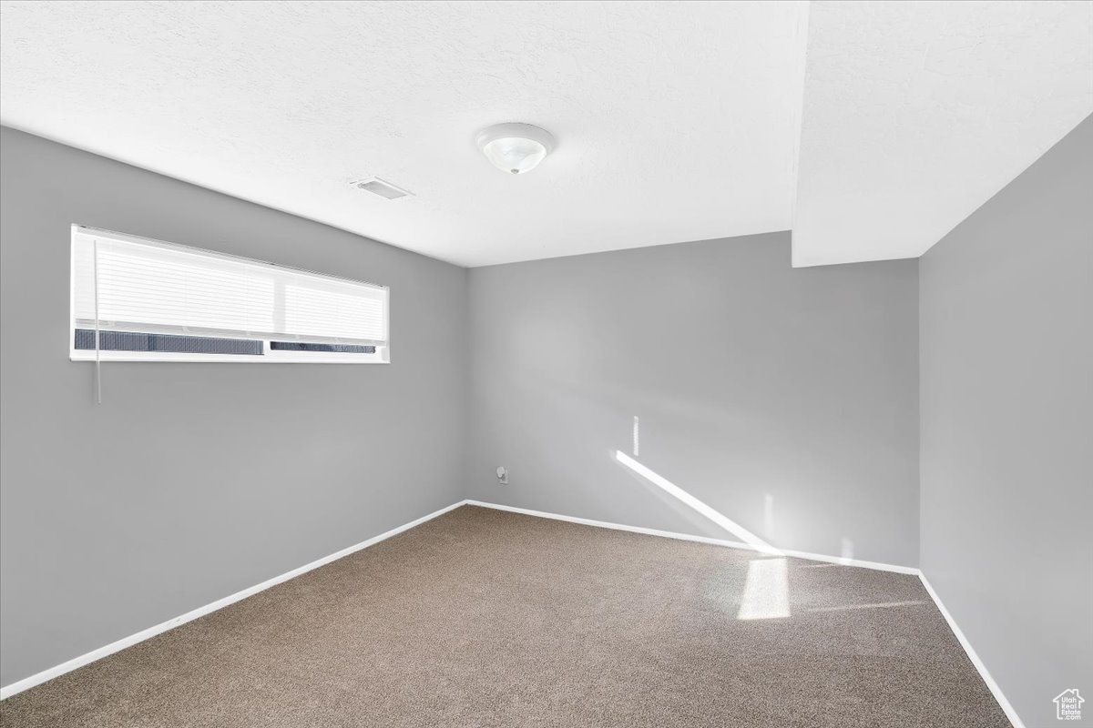 Unfurnished room with carpet flooring, visible vents, baseboards, and a textured ceiling