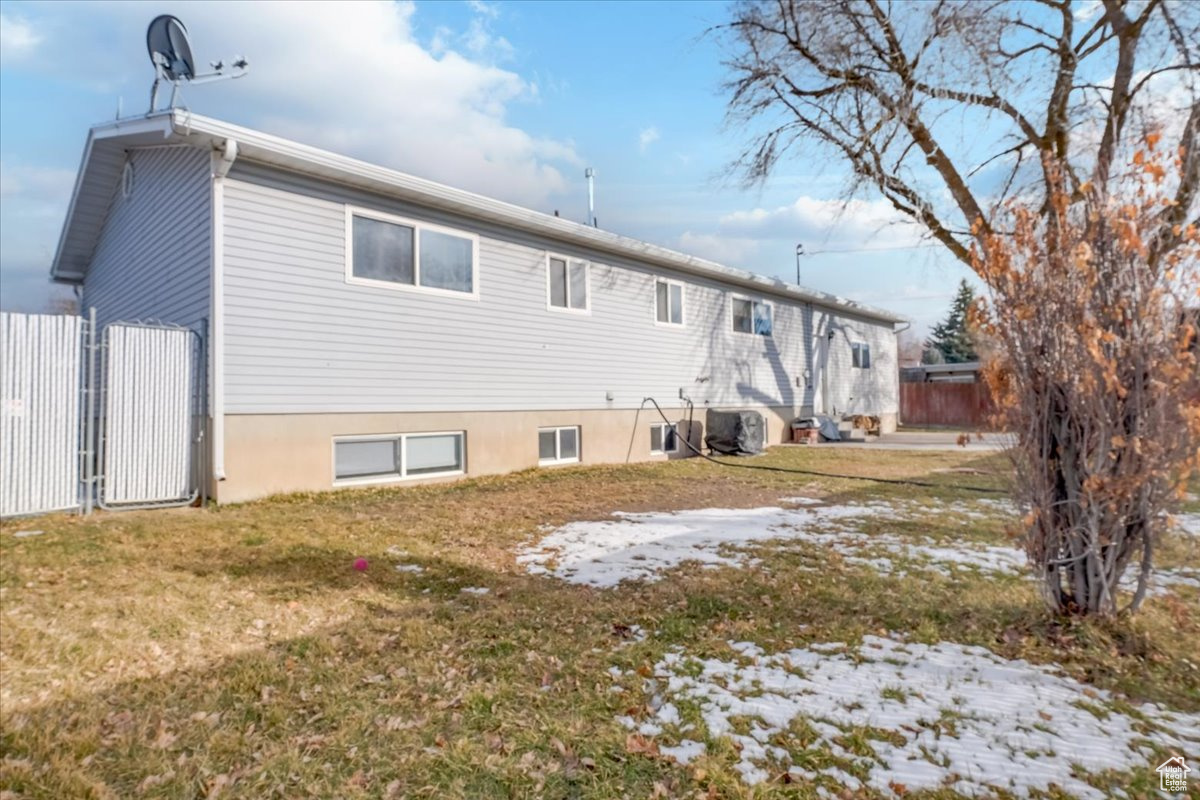 Back of property with central air condition unit, a lawn, and fence