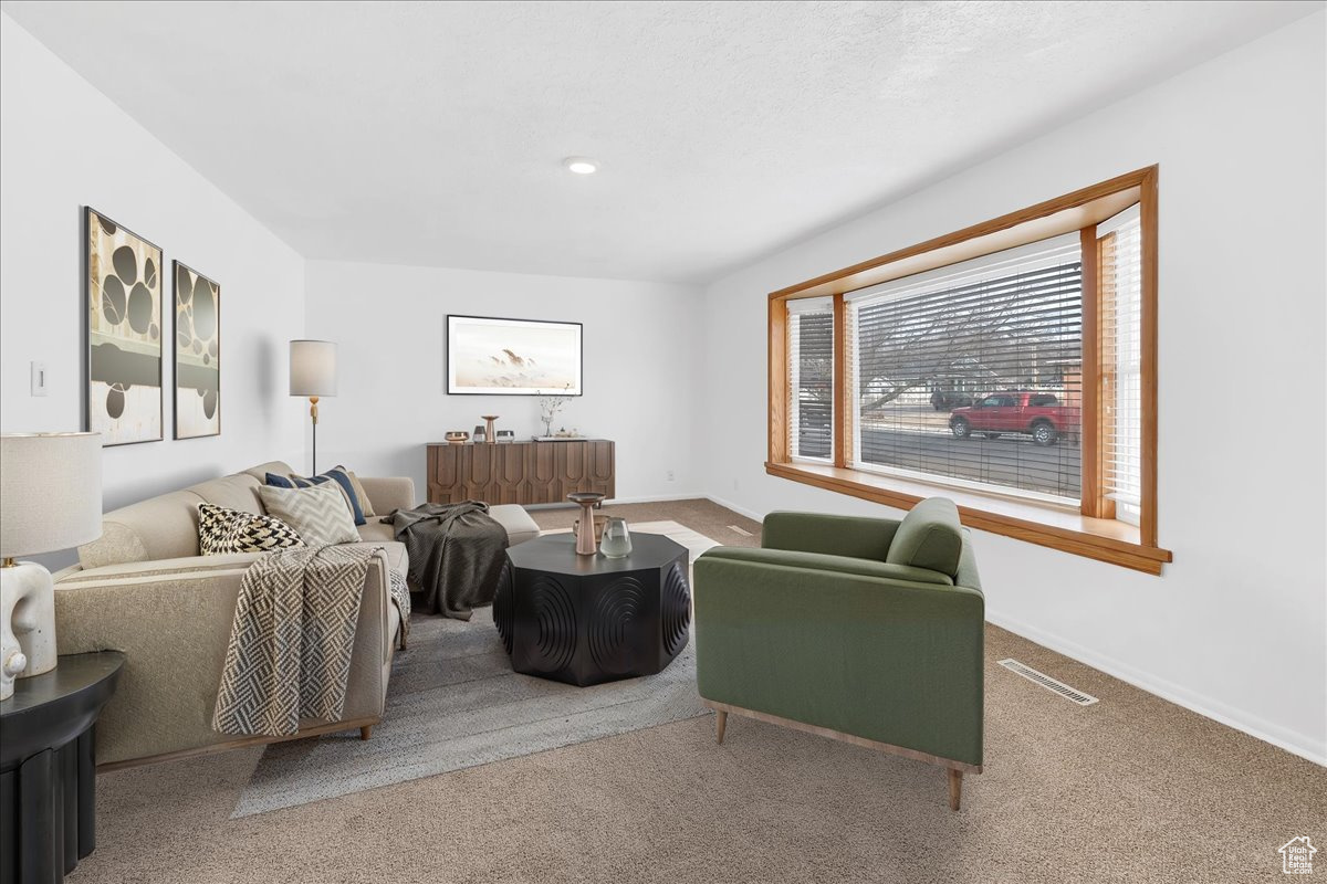 Living area featuring visible vents, baseboards, and carpet. Virtually staged.