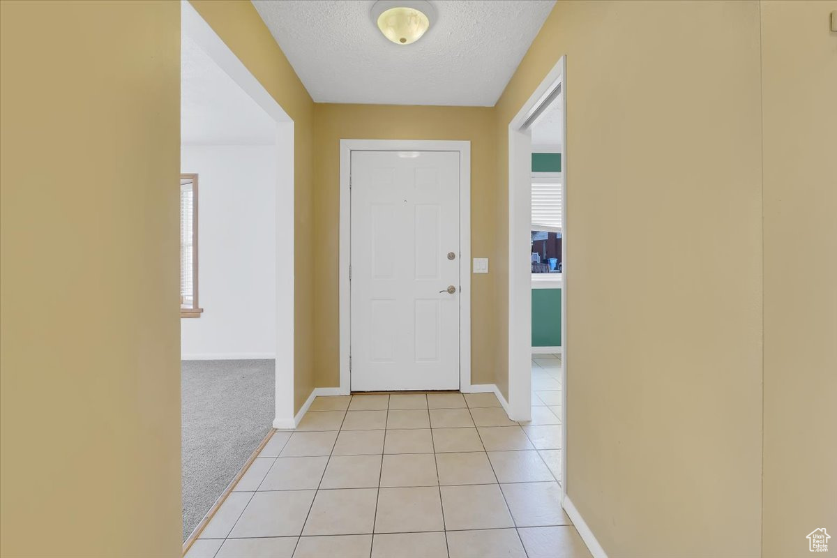 Entrance foyer featuring light carpet, light tile patterned floors, baseboards, and a textured ceiling