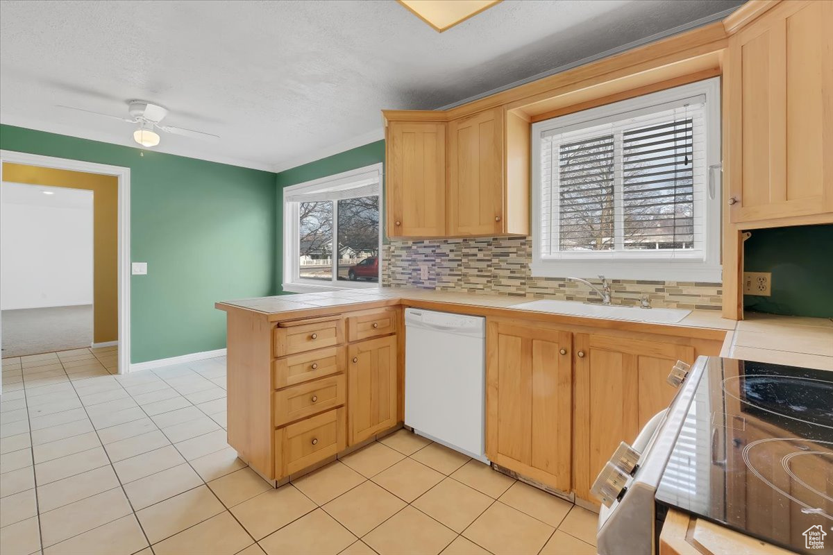 Kitchen with a sink, light brown cabinets, dishwasher, and tile countertops