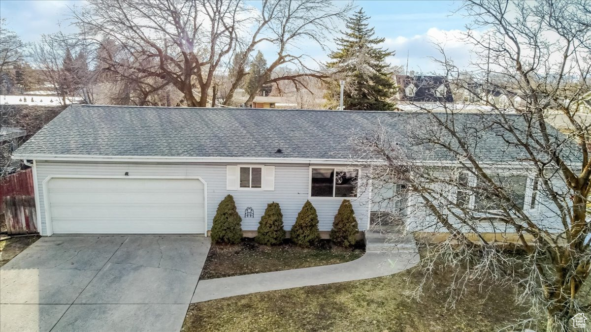 Exterior space with a garage, roof with shingles, driveway, and fence