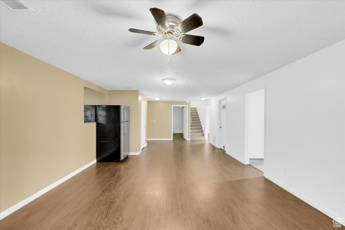 Unfurnished living room with wood finished floors, visible vents, baseboards, stairs, and a textured ceiling