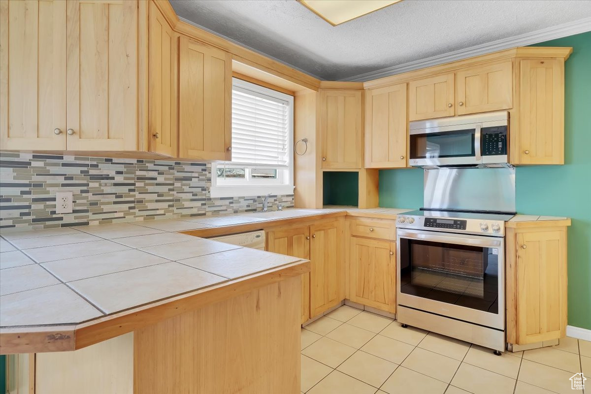 Kitchen featuring stainless steel appliances, backsplash, tile counters, and light brown cabinets
