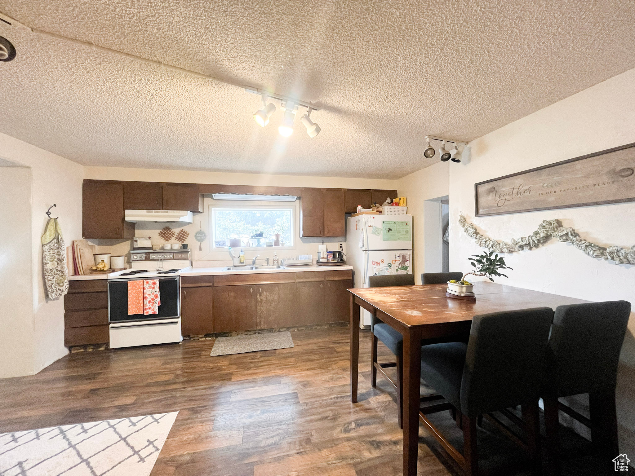 Kitchen featuring under cabinet range hood, light countertops, dark wood-style flooring, white appliances