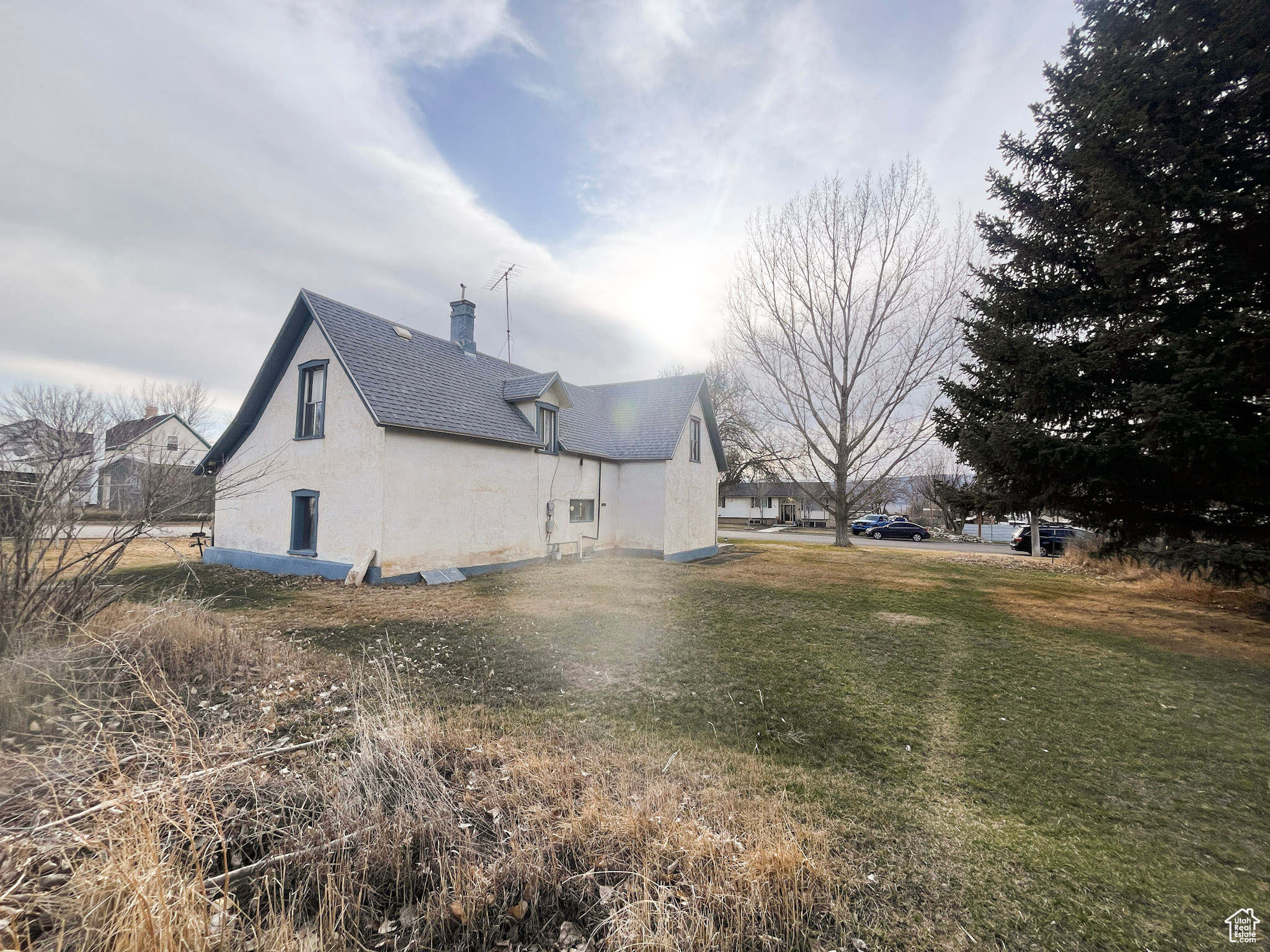 View of side of property with a lawn, a chimney, roof with shingles, and stucco siding