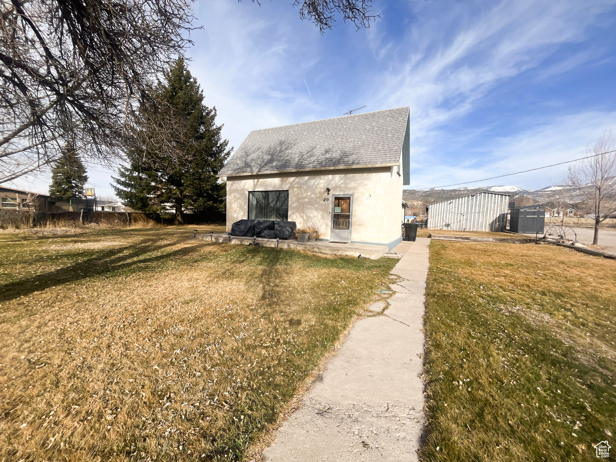 Exterior space featuring stucco siding, an outbuilding, roof with shingles, and a lawn