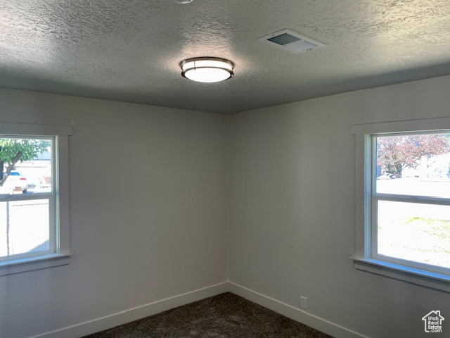 Unfurnished room featuring visible vents, baseboards, a textured ceiling, and dark carpet