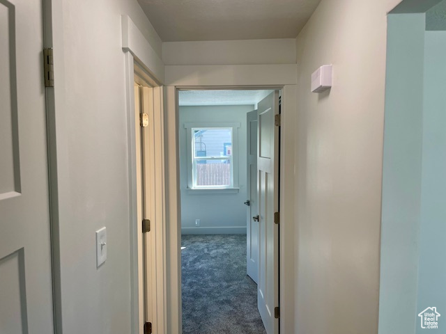 Hallway featuring dark colored carpet and baseboards