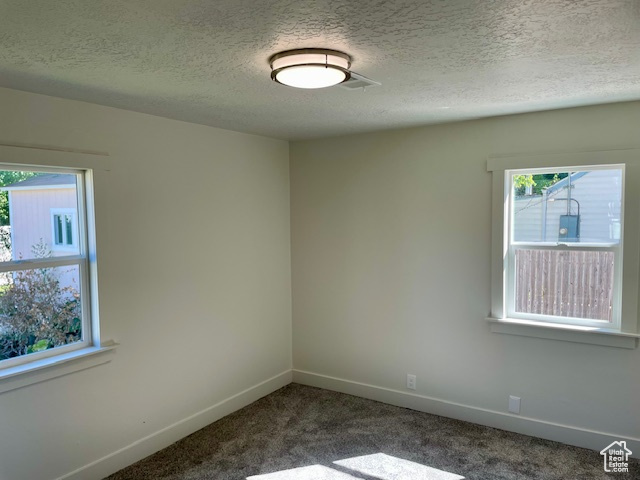 Empty room featuring baseboards, dark carpet, and a textured ceiling