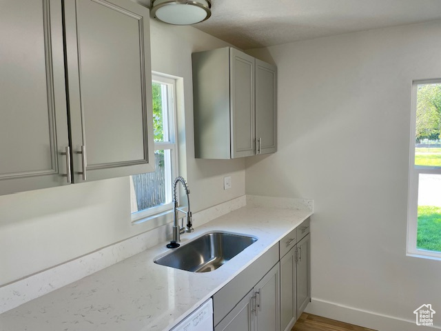 Kitchen with light stone counters, gray cabinets, baseboards, and a sink