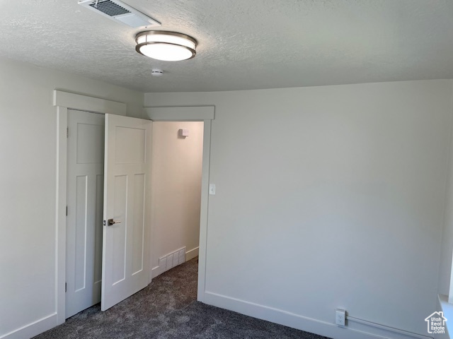 Empty room featuring visible vents, baseboards, dark colored carpet, and a textured ceiling