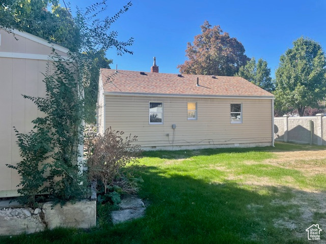 Rear view of house with crawl space, a lawn, a shingled roof, and fence