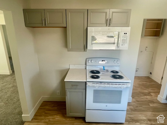 Kitchen featuring baseboards, white appliances, gray cabinetry, and wood finished floors