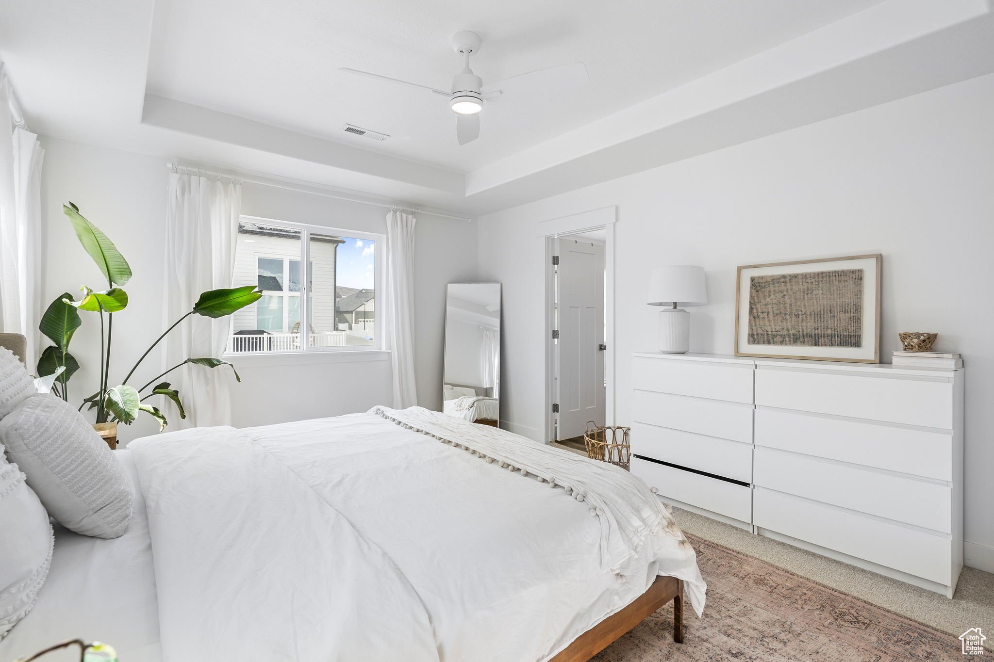 Bedroom with a raised ceiling, a ceiling fan, visible vents, and light carpet