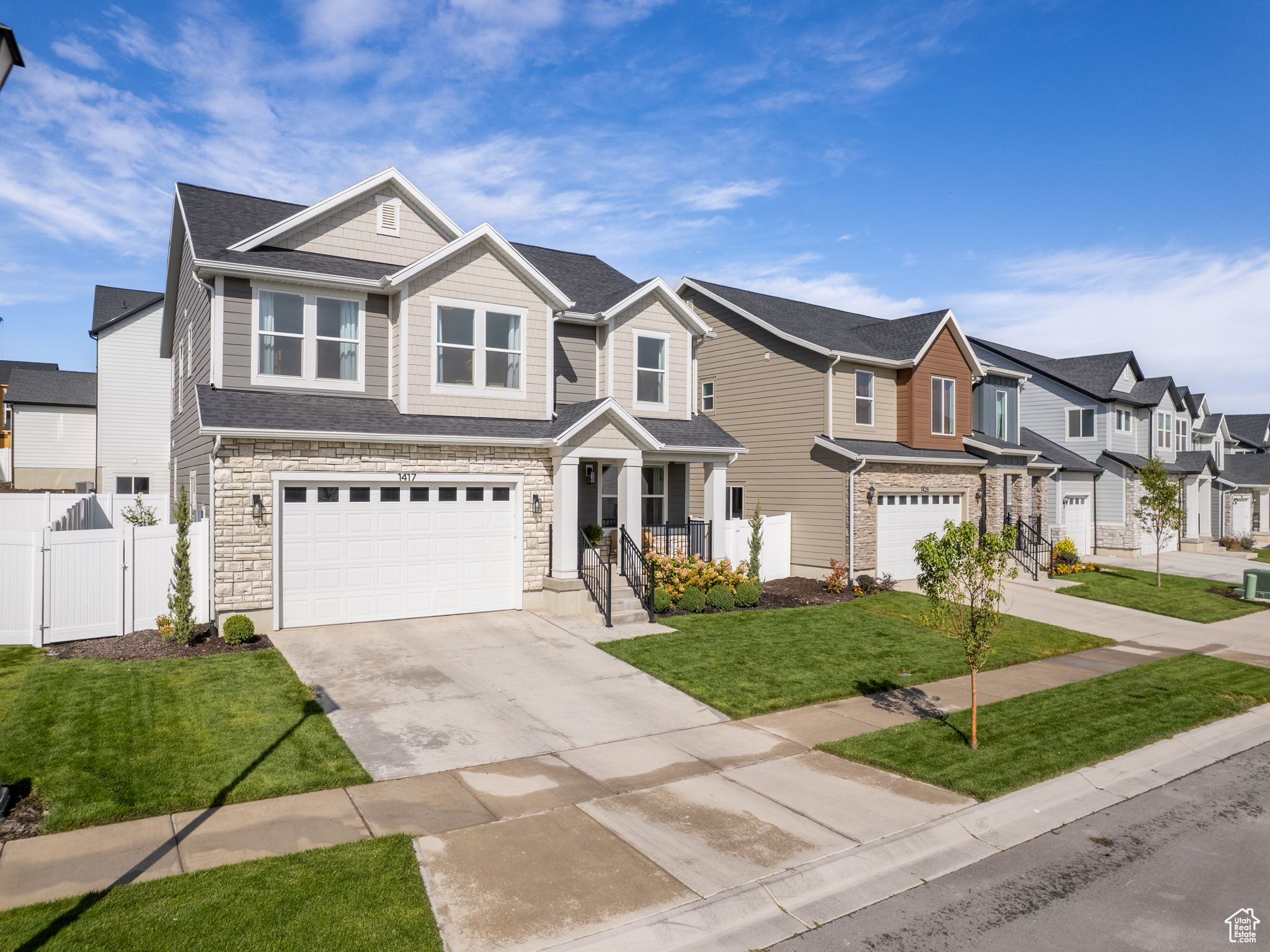 View of front of property featuring stone siding, fence, a residential view, concrete driveway, and a garage